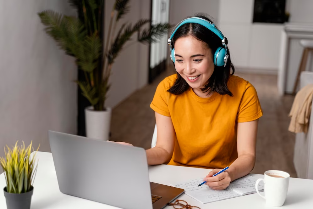 A smiling girl wearing a headset, holding a pen in front of a laptop