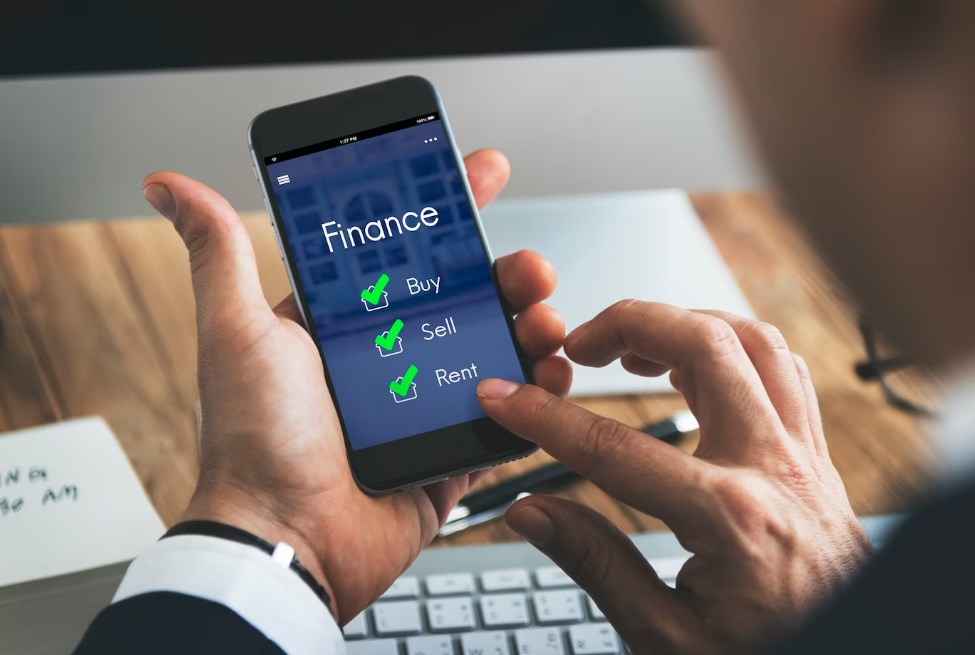 two hands holding a smartphone displaying a finance app with buy, sell, and rent options